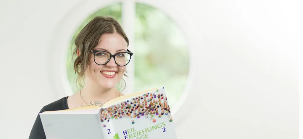 Lächelnde APS Auszubildende hält ein Buch über die Heilerziehungspflege
