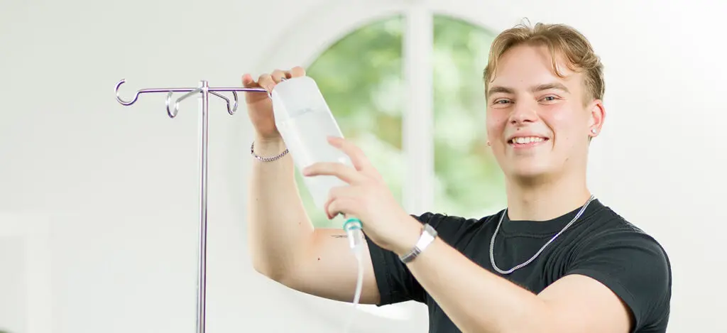 Lächelnder Auszubildende befestigt eine Flasche an einem Tropf