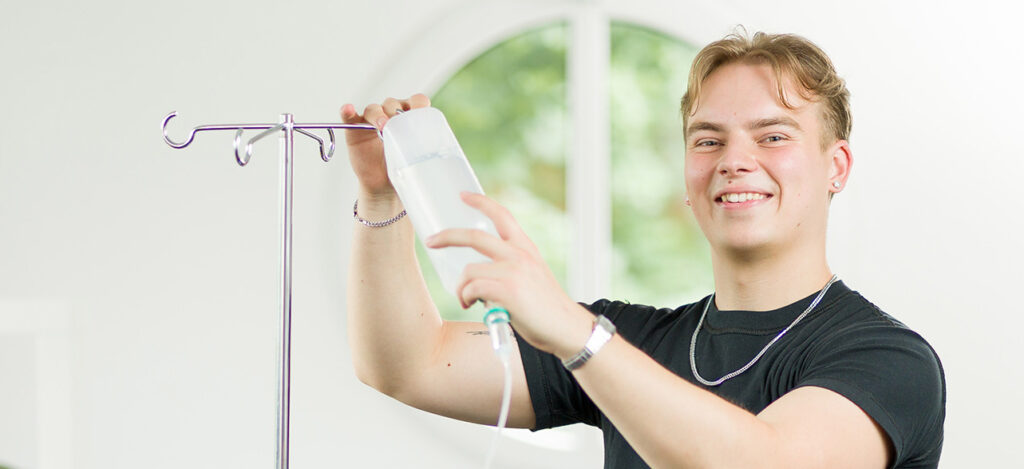 Lächelnder Auszubildende befestigt eine Flasche an einem Tropf