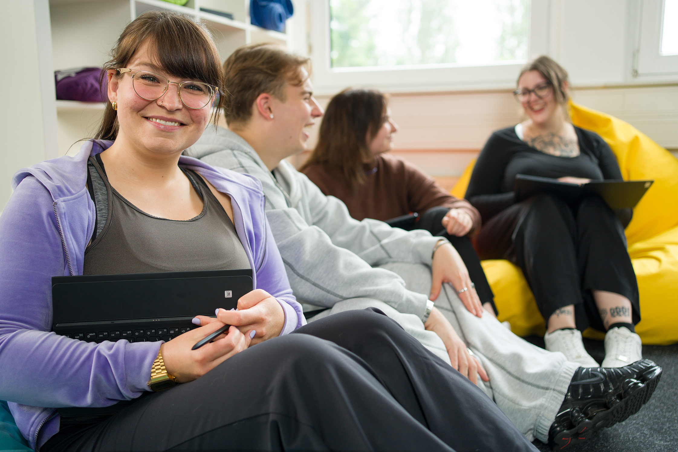 Auszubildende zur Pflegefachfrau hält ein Tablet im Arm und lächelt in die Kamera